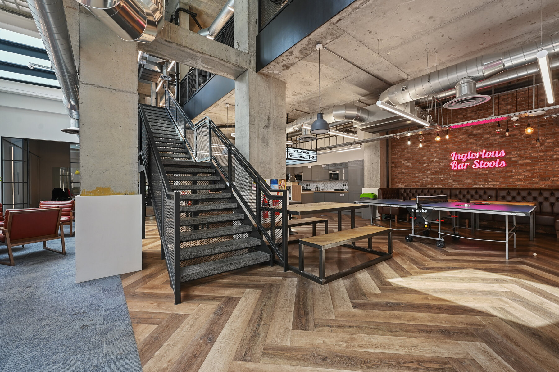 Double-height social workspace with exposed services and a central steel stair